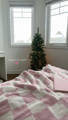 a pink and white blanket sitting on top of a bed next to a christmas tree