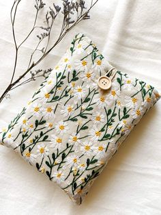 a white and yellow flowered pillow with a button on it next to a plant