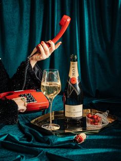 a woman holding a red phone next to a bottle of wine and two glasses on a tray