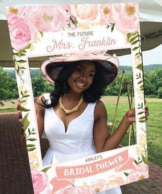 a woman in a white dress and hat holding up a pink flowered photo frame