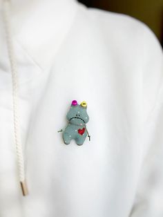 a close up of a person wearing a white shirt with a frog brooch on it