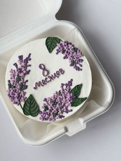 there is a cake with purple flowers on it in a white box that says welcome