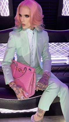 a woman with pink hair and tattoos sitting on a chair holding a pink handbag