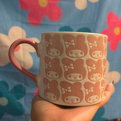 a hand holding a coffee cup with bear designs on it, in front of a flowery background