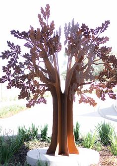 a metal tree sculpture sitting on top of a white pedestal next to grass and bushes