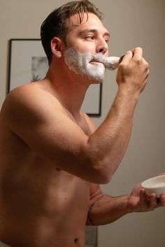 a shirtless man shaving his face with a razor and toothpaste on