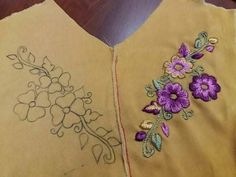 two embroidered vests with flowers on them sitting on top of a wooden table next to a pair of scissors