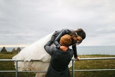 a bride and groom hugging on the side of a fence near the ocean in iceland