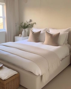 a large white bed sitting in a bedroom next to a window with lots of pillows on top of it