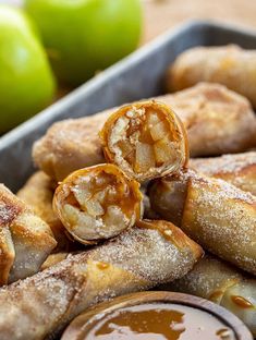 some food is sitting in a tray on a table next to apples and dipping sauce