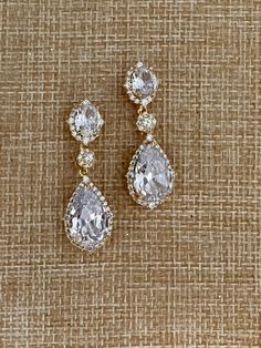 two pairs of diamond earrings sitting on top of a piece of burloom cloth