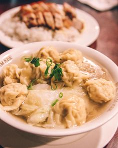 two white bowls filled with dumplings and meat on top of a wooden table next to rice