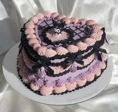 a three layer cake decorated with pink and purple icing, black laces and a teddy bear on top