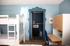 a bedroom with bunk beds and desks in the corner, next to a blue wall