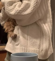 a cat is wrapped up in a sweater next to a coffee mug