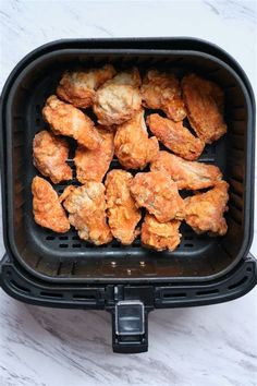 chicken wings in an air fryer on a white marble counter top, ready to be cooked