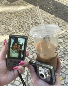 a woman holding a camera and taking a picture with her cell phone next to a cup of coffee