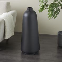 a black vase sitting on top of a wooden floor next to a white chair and potted plant