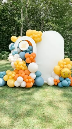 a large balloon arch with balloons on it in the middle of a grassy area next to trees