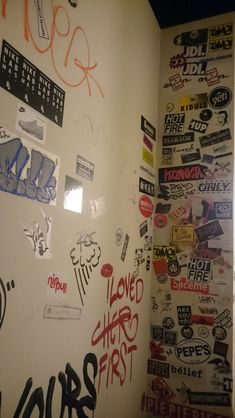 the wall has many stickers on it and is white with black writing in different colors