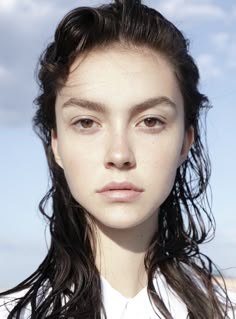 a close up of a person wearing a white shirt with long hair and blue sky in the background