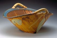 a brown and blue bowl with a wooden handle on the top, sitting on a gray surface