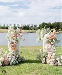 two tall vases with flowers are sitting in the grass near some water and trees