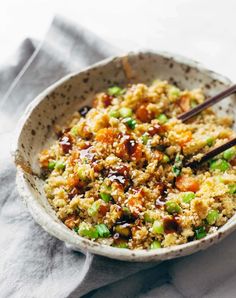 a bowl filled with rice and vegetables on top of a table next to chopsticks