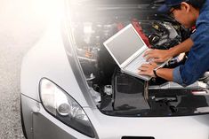 a man working on his laptop under the hood of a car