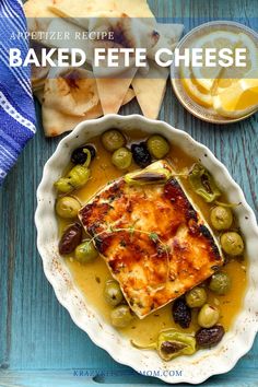 baked feta cheese with olives in a bowl next to crackers and bread