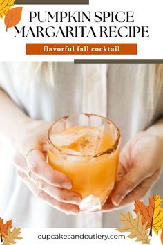 a person holding a glass filled with orange liquid and topped with an orange slice, surrounded by fall leaves