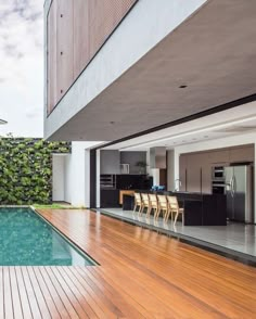 an outdoor kitchen and dining area with wooden flooring next to a swimming pool in a modern home