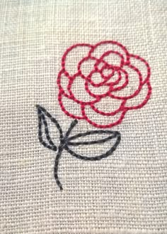 a red rose is embroidered on a white piece of cloth with black stitching around it