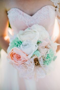 the bride's bouquet was made with white and peach flowers, green leaves, and lace