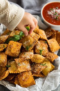 someone is picking up some fried food from a basket with dipping sauce on the side