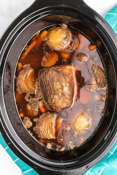 a slow cooker filled with stew and meatballs on top of a blue towel