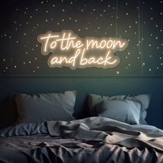 a neon sign that says to the moon and back on a wall above a bed