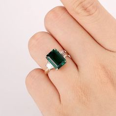 a woman's hand holding an emerald and diamond ring on top of her finger