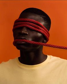 a man with red rope tied to his head and neck, in front of an orange background