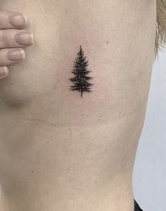 a small pine tree tattoo on the back of a woman's left side ribcage