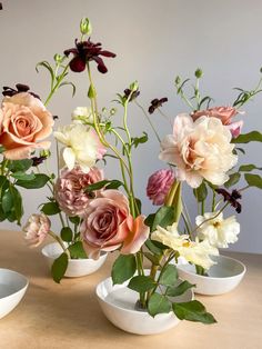 three vases filled with different types of flowers on top of a wooden table next to bowls