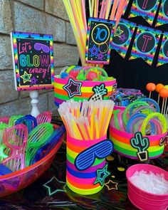 a table topped with lots of neon colored plastic cups filled with candy and lollipop sticks