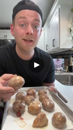 a man is holding up some doughnuts on a baking sheet in the kitchen