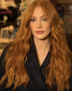 a woman with long red hair is posing for a photo in front of a camera