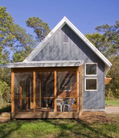 a small gray house sitting on top of a lush green field next to a forest