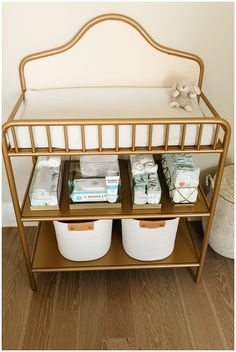 a gold metal shelf with three baskets on top and two white plastic containers under it