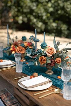 the table is set with blue and orange flowers in vases, silverware, and candlesticks