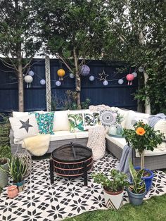 an outdoor seating area with potted plants and decorative pillows on the couches, in front of a blue fence