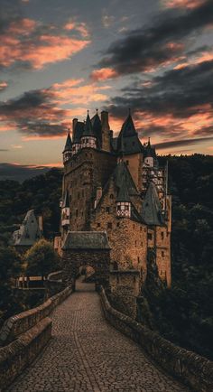 an old castle sitting on top of a hill next to a river under a cloudy sky