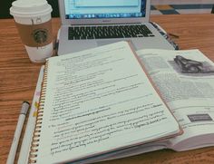 an open book sitting on top of a wooden table next to a laptop computer and cup of coffee